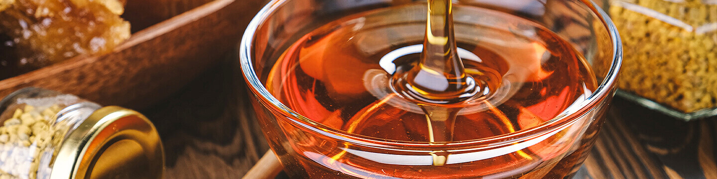 Golden honey drips into jar of honey