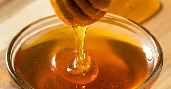 Golden honey drips into jar of honey