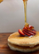 Good quality raw honey being poured over pancakes with strawberries
