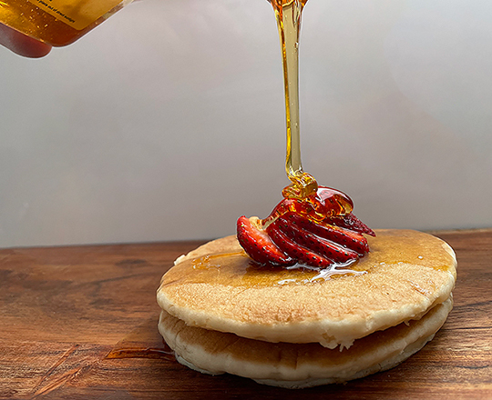 Good quality raw honey being poured over pancakes with strawberries